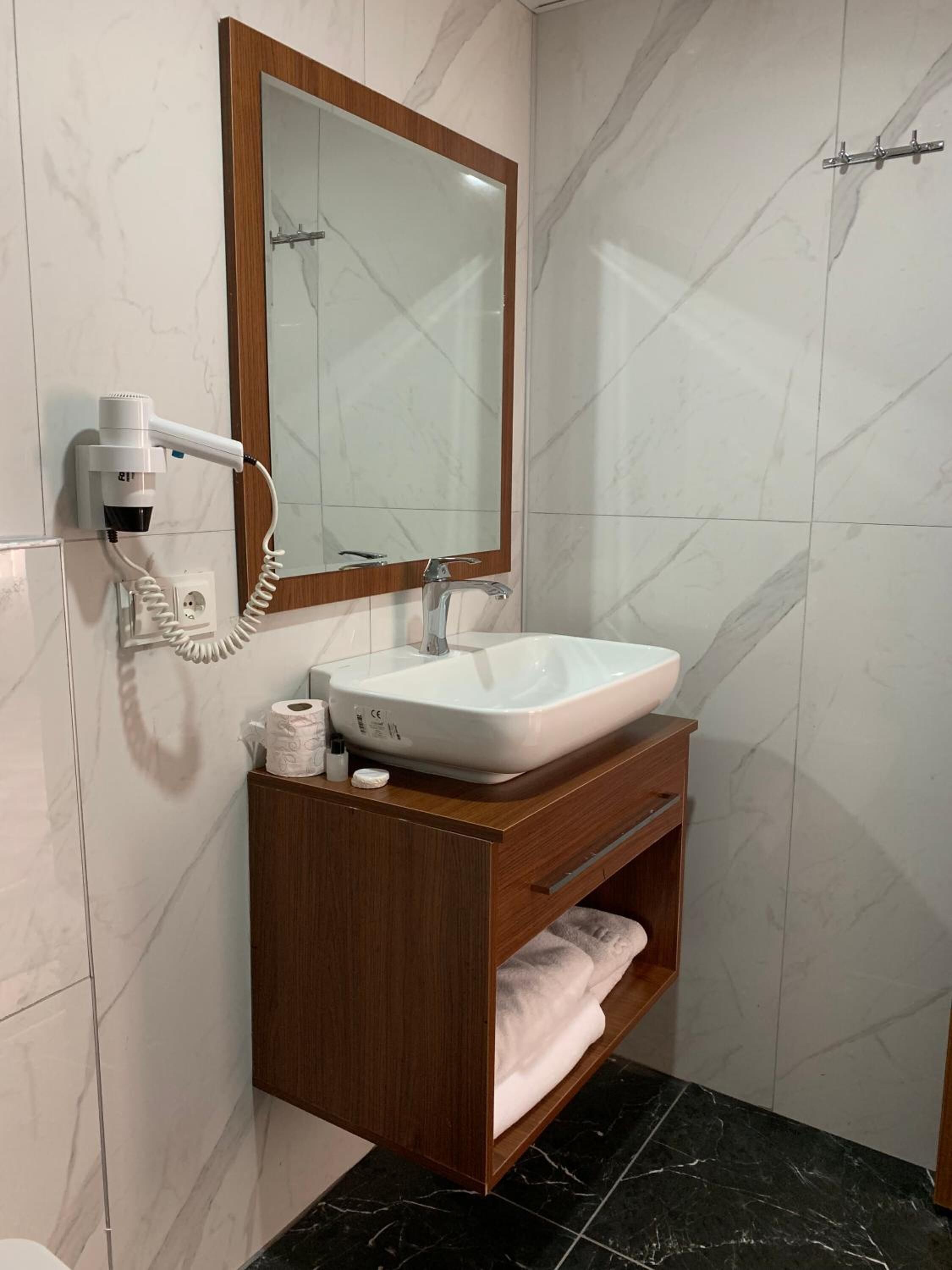 Un baño con un lavabo blanco, un tocador de madera, un espejo y un secador de pelo en la pared.