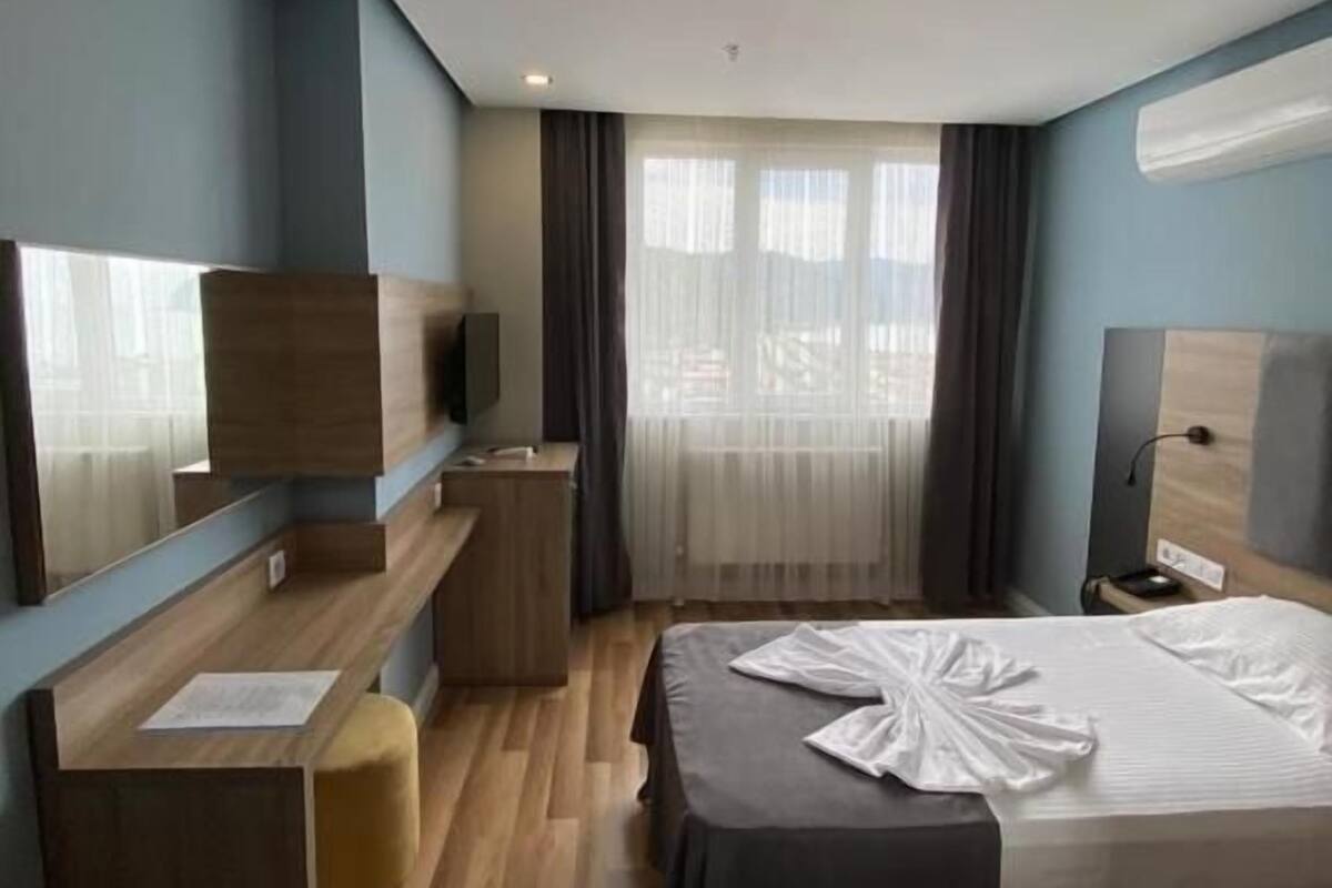 A modern hotel room with a bed, a desk, a chair, a TV, and a window with curtains.