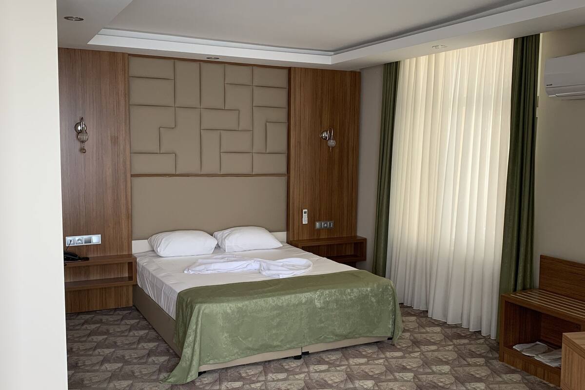 A hotel room with a bed, a wooden wardrobe, a bedside table, a bench, and a patterned carpet.