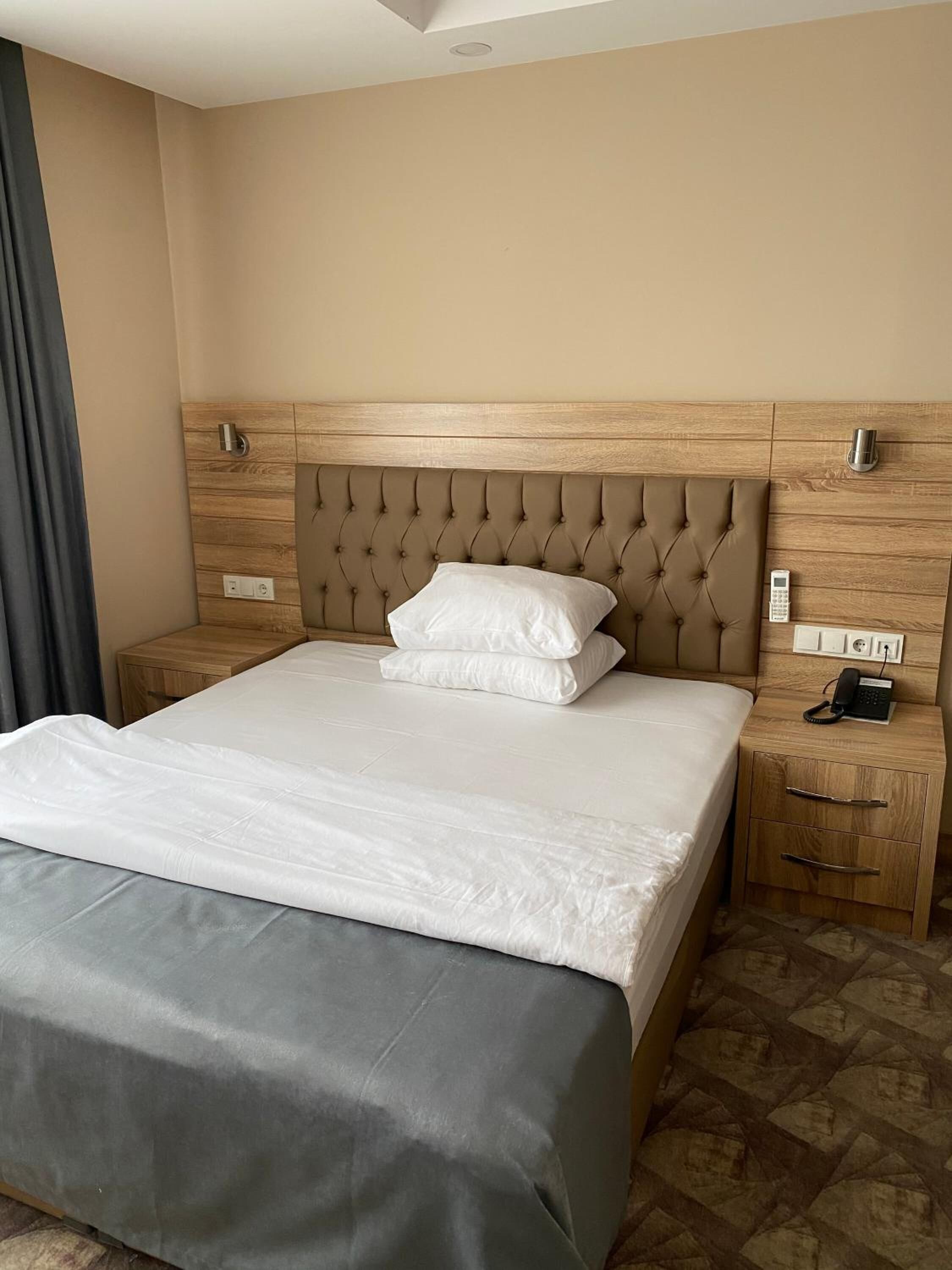 A hotel room with a large bed, wooden headboard, bedside tables with phones, and a patterned floor.
