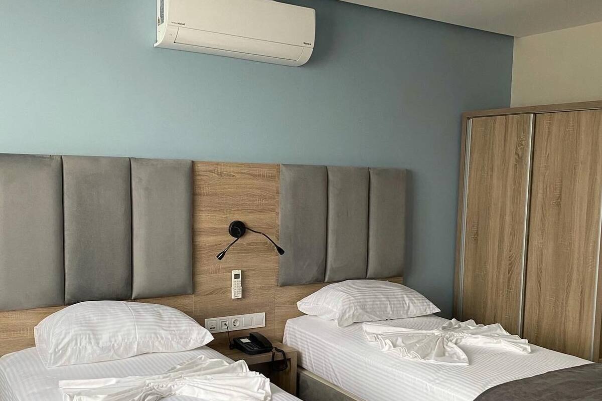 A hotel room with two beds, a wooden headboard, a bedside table with a phone, and an air conditioning unit.