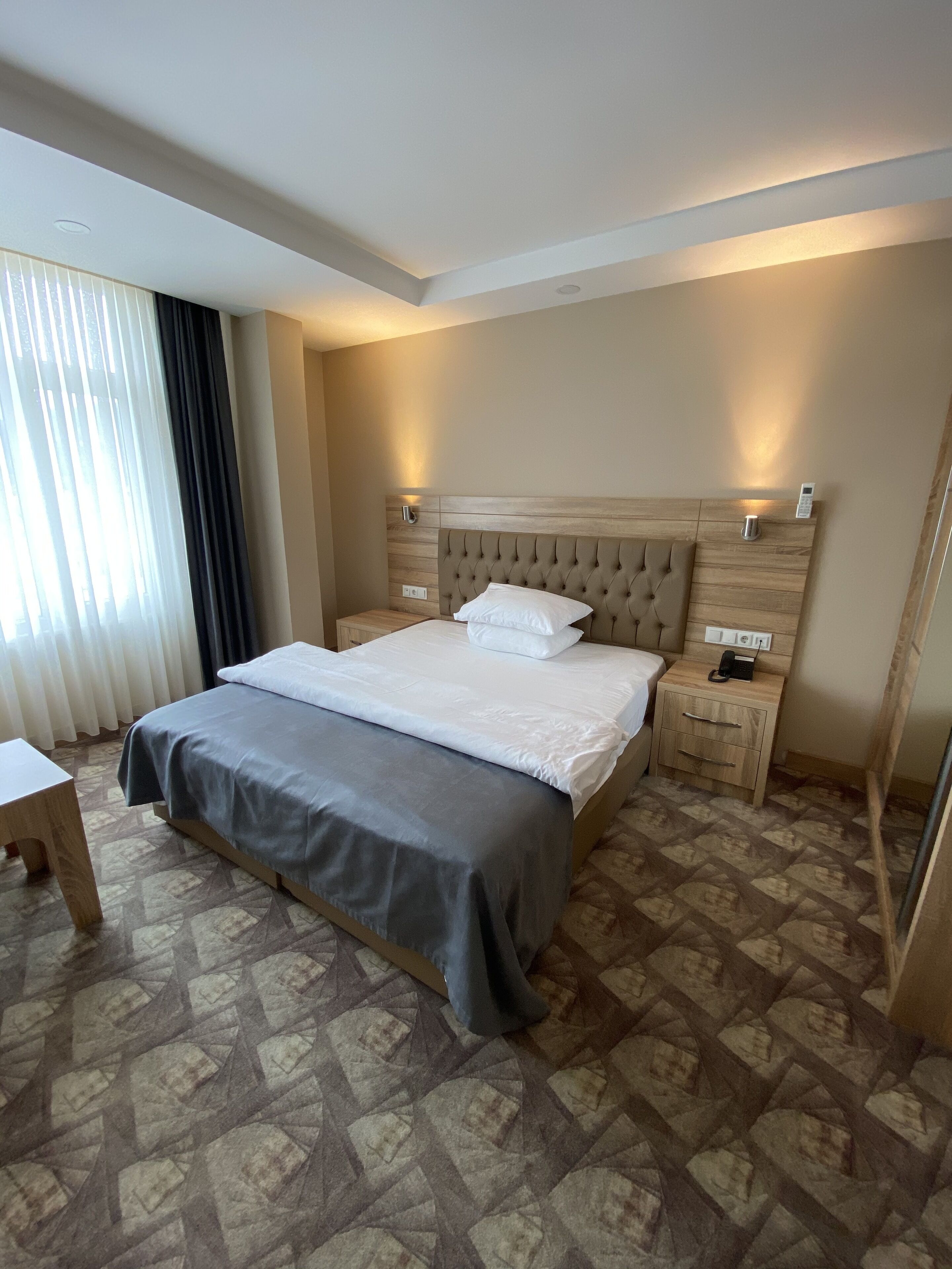 A hotel room with a large bed, bedside tables, a desk, and a mirror.
