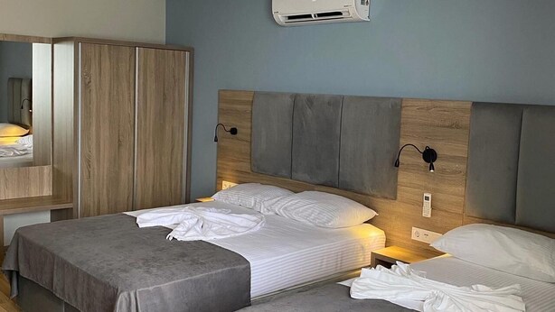 A modern hotel room with two beds, a wardrobe, a mirror, and an air conditioning unit.