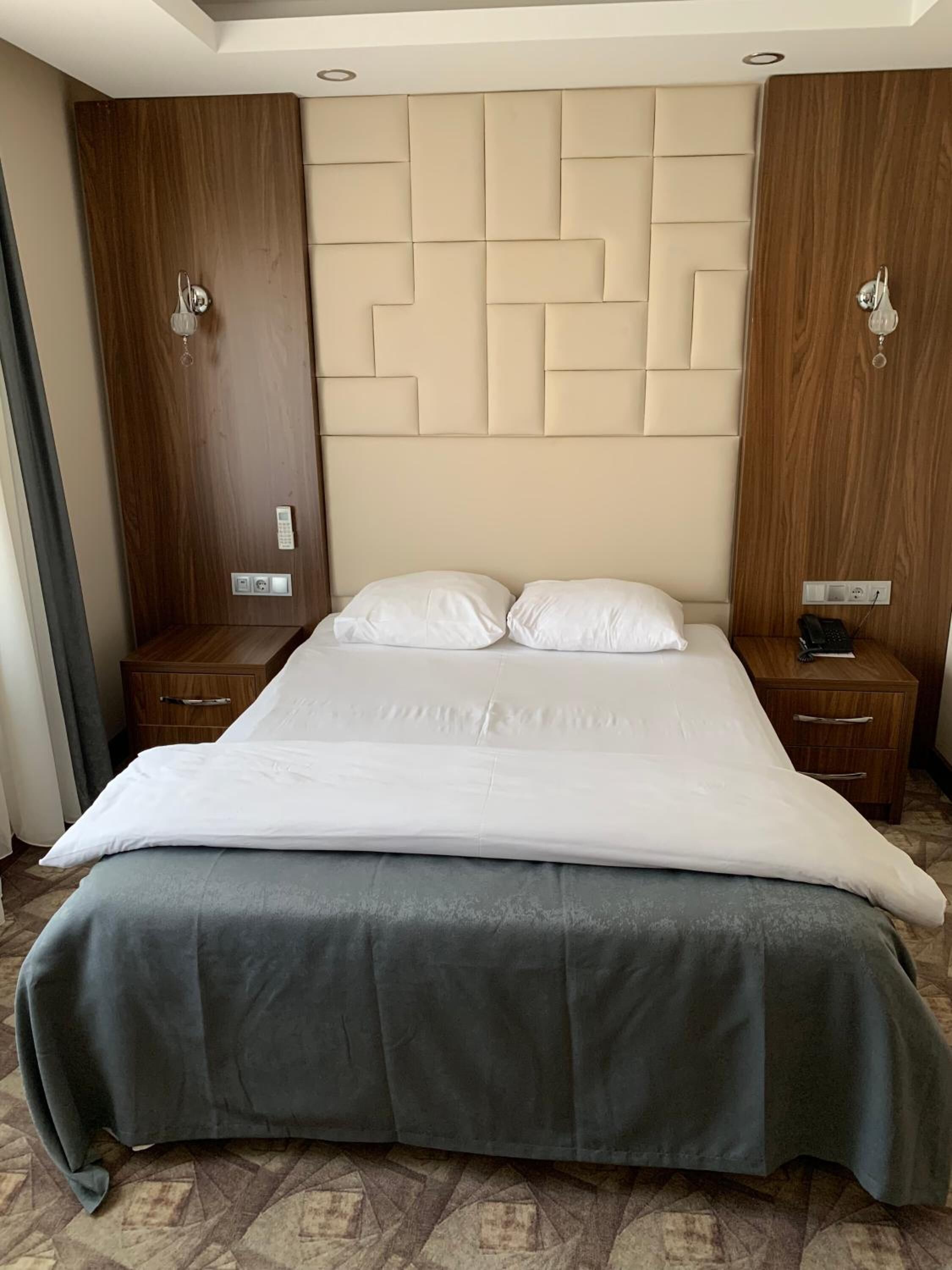 Une chambre d’hôtel avec un grand lit, une tête de lit en bois et deux tables de chevet avec des lampes.