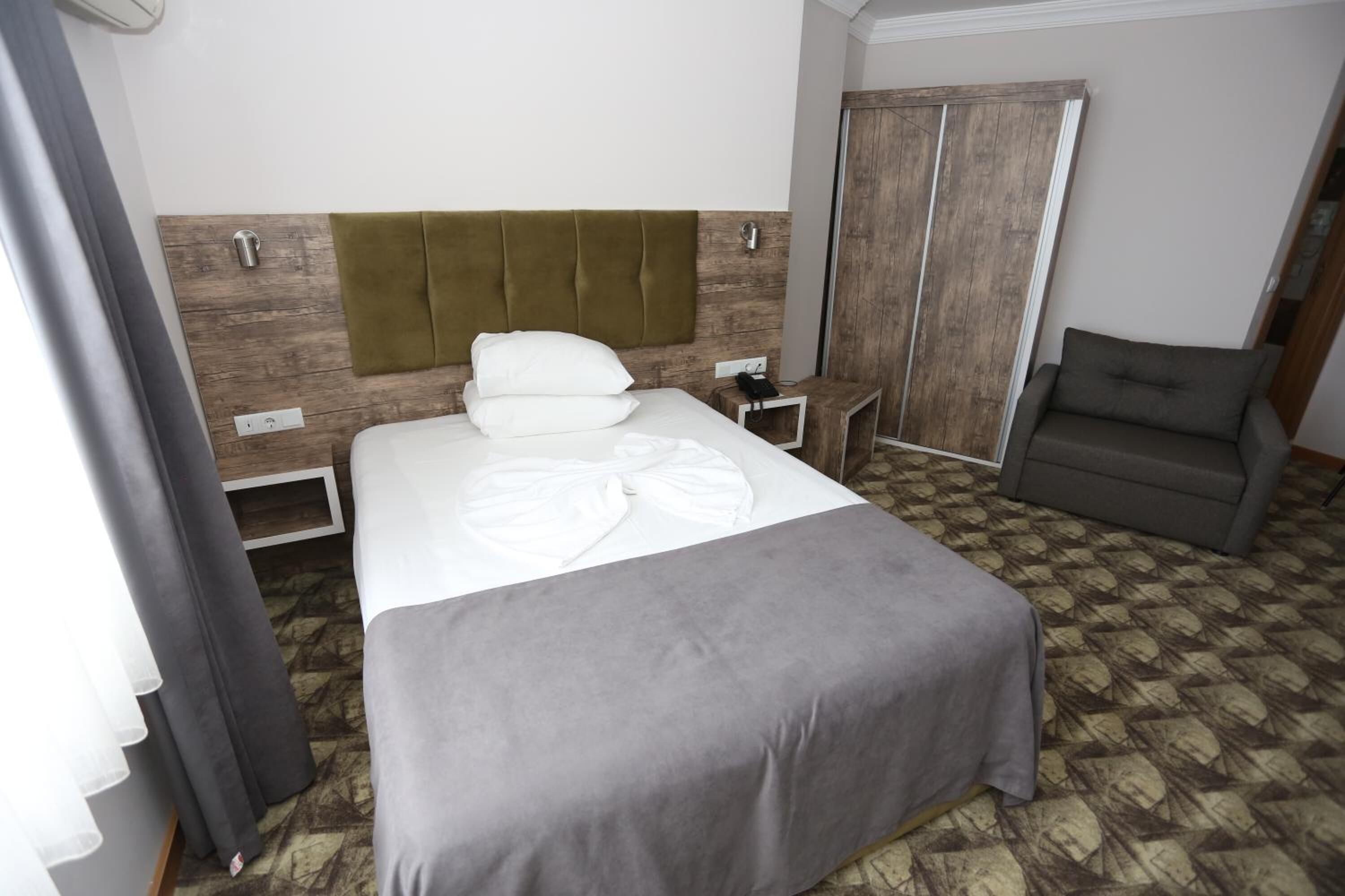 Een hotelkamer met een bed, nachtkastje, stoel en garderobe.