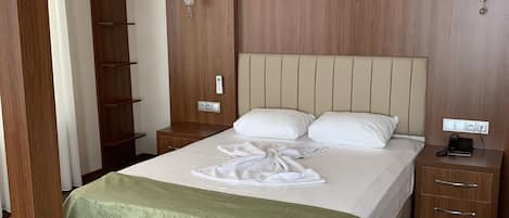 A neatly made bed with a green bedspread, wooden paneling on the walls, a bedside table with a phone, and a wall-mounted light fixture.