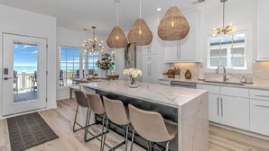 A modern kitchen with a large island, pendant lights, and a view to the outside.