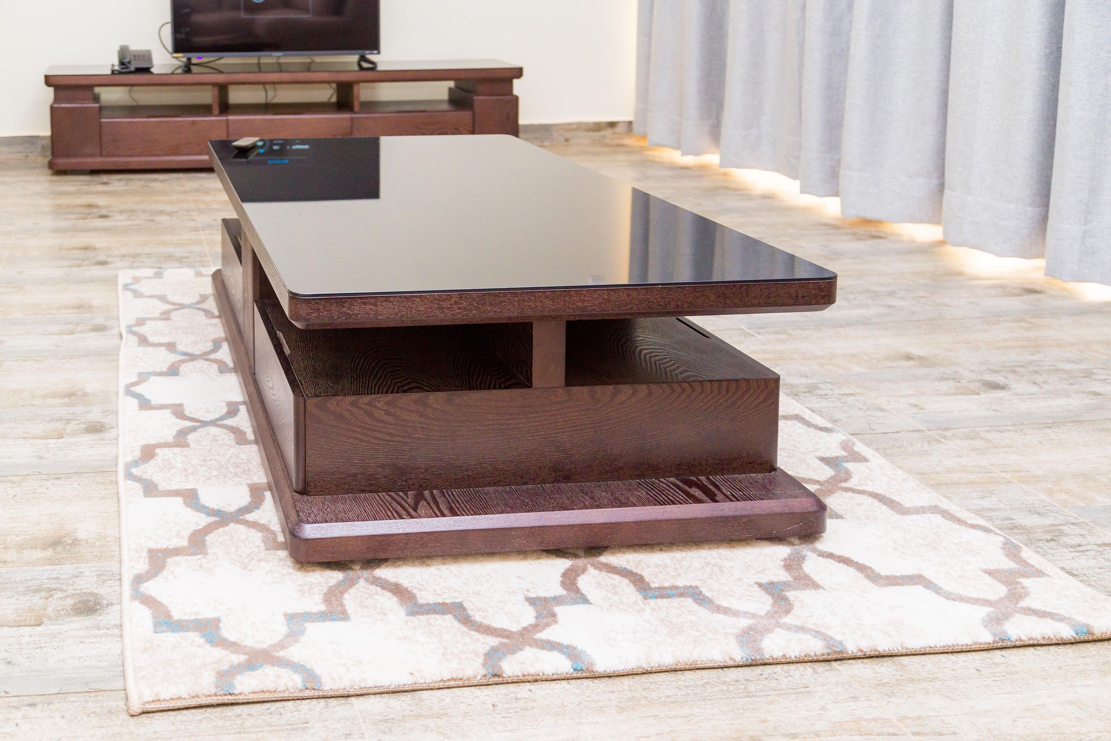 A modern living room with a glass-top coffee table, wooden side tables, and a patterned rug.