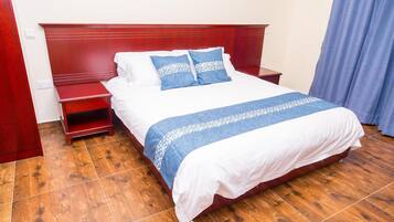 A neatly made bed with a white and blue bedspread, a wooden headboard, and a wooden nightstand with a red finish.