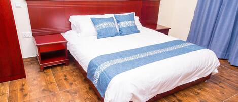 A neatly made bed with a white and blue bedspread, a wooden headboard, and a wooden nightstand with a red finish.