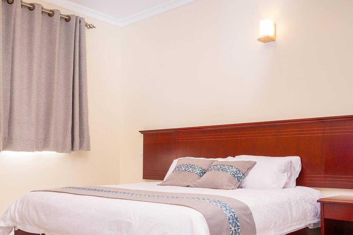 Una cama bien hecha con cabecera de madera, una mesita de noche y una lámpara de pared.