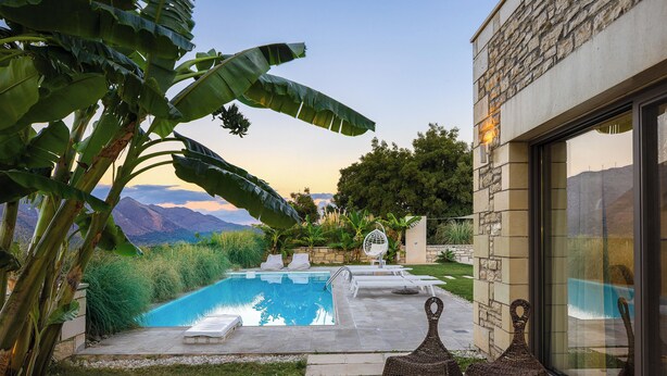 A pool area with lounge chairs, a stone building, and a view of mountains.