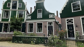 Uma fileira de casas tradicionais com fachadas verdes e detalhes brancos, apresentando detalhes em tijolo e um pequeno jardim com cerca.