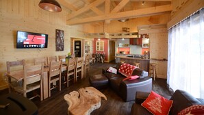 Un vaste espace de vie doté d’un plafond en bois, d’un ensemble de salle à manger, d’un canapé et d’une cuisine à l’arrière-plan.