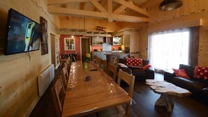 Un intérieur en bois comprenant une table à manger, des chaises, un canapé et un téléviseur fixé au mur.