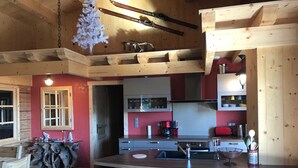 Une cuisine chaleureuse avec des poutres en bois, un coin bar avec des tabourets et un mur d’accent rouge.
