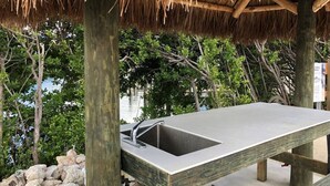 A metal sink with a faucet under a wooden structure with a thatched roof, surrounded by greenery and rocks. - Dbl Master |Oceanview |Jacuzzi |Beach |Marina |BBQ (Tavernier)