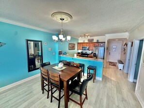 A dining area with a wooden table and chairs, a kitchen with wooden cabinets and stainless steel appliances, and a hallway leading to other rooms.