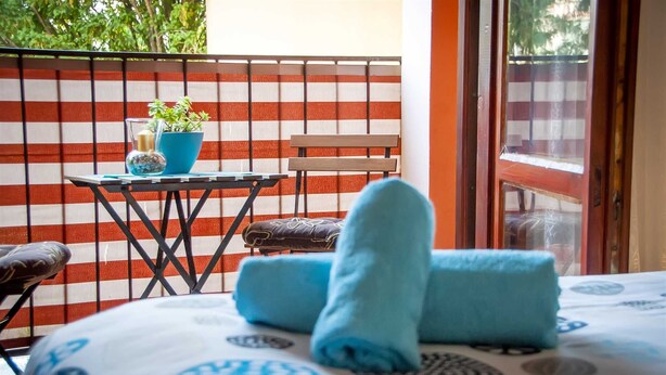 Un balcón con una pared a rayas, una mesita con una planta en maceta, una silla y una cama con toallas azules.