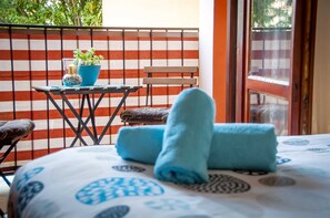 A balcony with a striped wall, a small table with a potted plant, a chair, and a bed with blue towels.