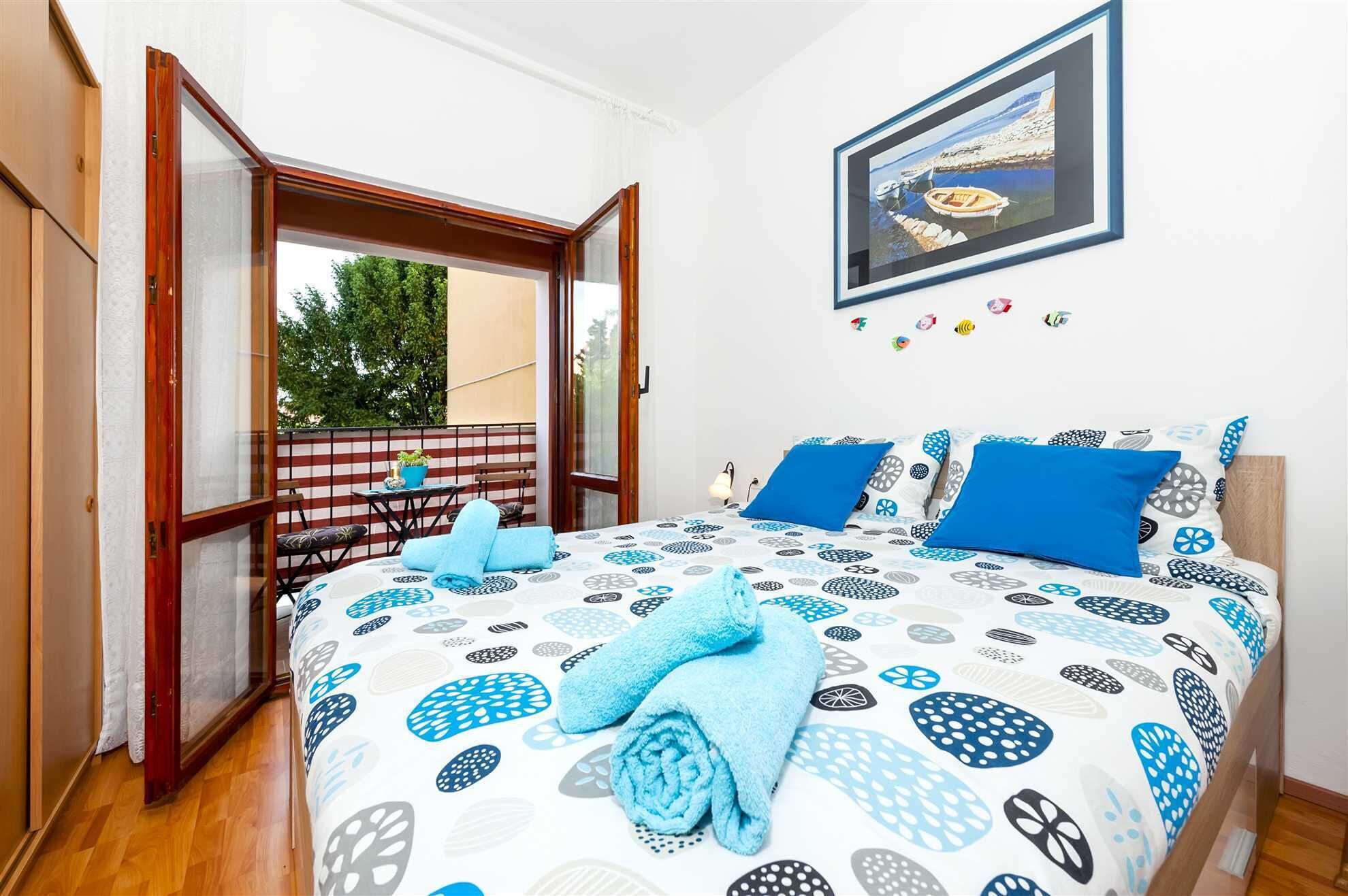 A bedroom with a bed, a window, a painting, and a balcony.