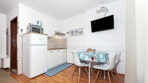 Cocina compacta con refrigerador, microondas y estufa, una mesa de comedor con sillas y un televisor de pantalla plana montado en la pared.