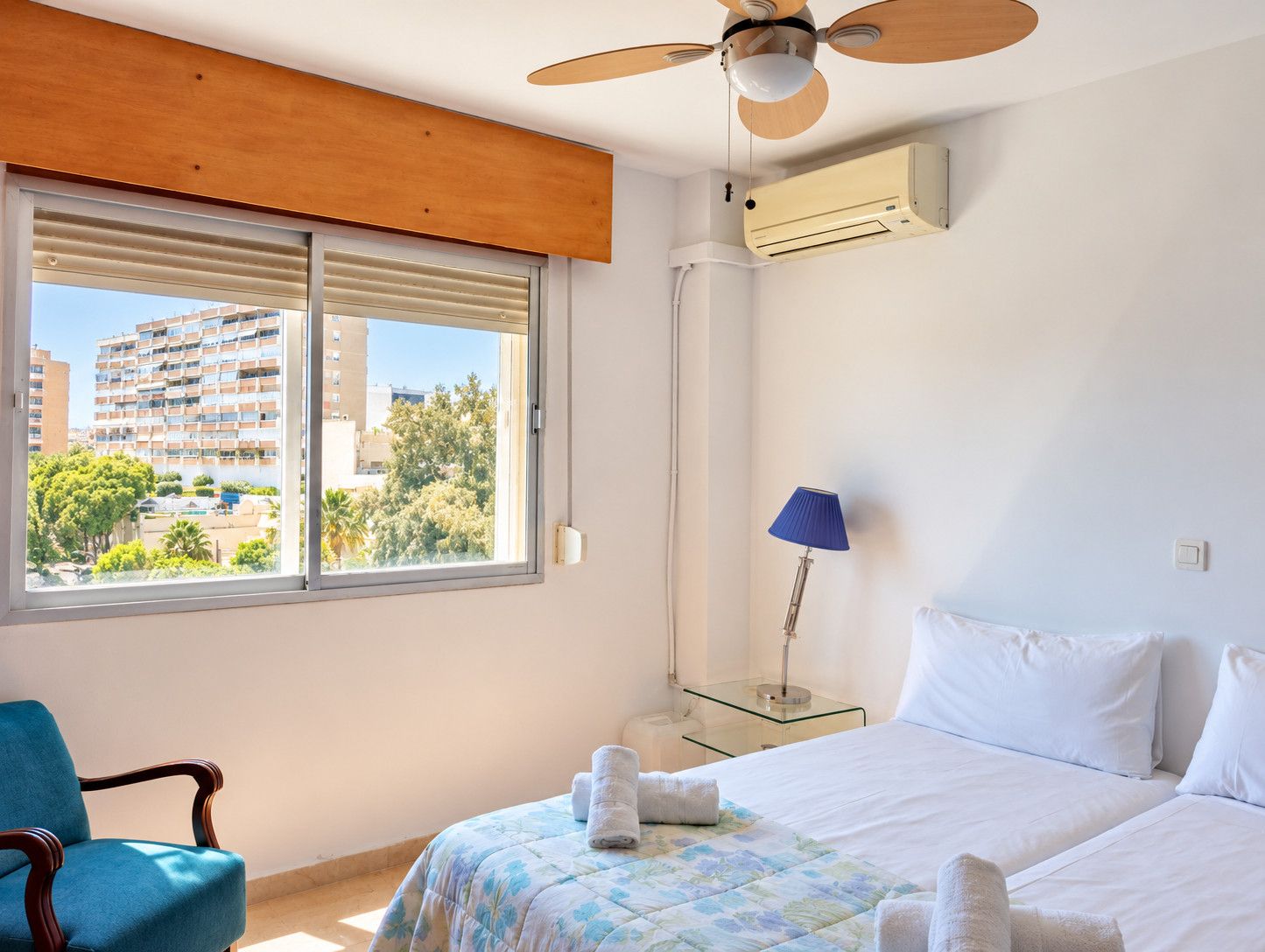 Ein Hotelzimmer mit Bett, Stuhl, Lampe und Blick auf ein Gebäude durch das Fenster.