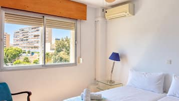 Ein Hotelzimmer mit Bett, Stuhl, Lampe und Blick auf ein Gebäude durch das Fenster.