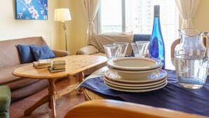 A hotel room with a sofa, a small table with books, a stack of plates, a blue bottle, and a pitcher. - MalagaSuite Beautiful Coast (Torremolinos)