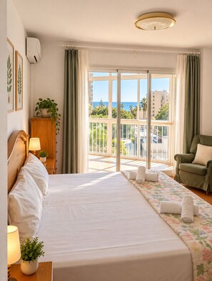 A hotel room with a bed, a chair, a desk, a potted plant, and a view of the sea. - MalagaSuite Beautiful Coast (Torremolinos)