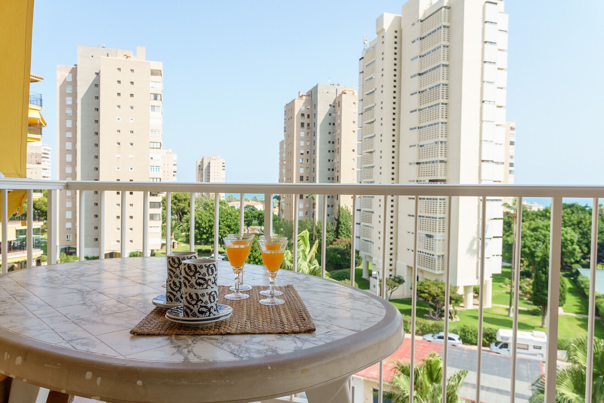 Un balcon avec une table dressée pour deux personnes, agrémentée de vaisselle à motifs et de deux verres contenant une boisson à l’orange.
