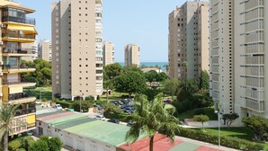 A high-rise residential building with multiple balconies, a green sports court, and a palm tree in the foreground. - MalagaSuite Beautiful Coast (Torremolinos)