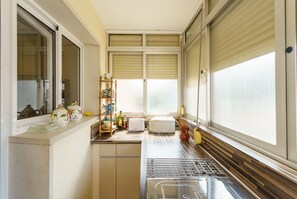 A compact kitchen with a built-in oven, a drying rack, and a window with blinds.