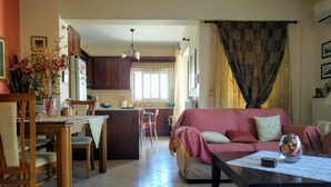 A cozy living room with a sofa, a dining table, and a kitchen in the background. - Thalia Apartment Kalamata (Kalamata)