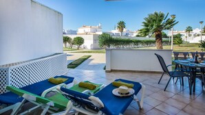 Un balcón con sillones de descanso, una mesa y vistas a edificios y palmeras.