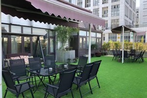 Un espacio de estar al aire libre con una mesa y sillas de vidrio, rodeado de un césped verde y la fachada de un edificio.