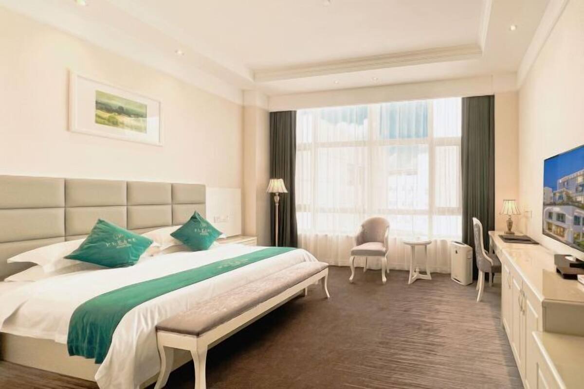 A hotel room with a large bed, a desk, a chair, and a window with curtains.