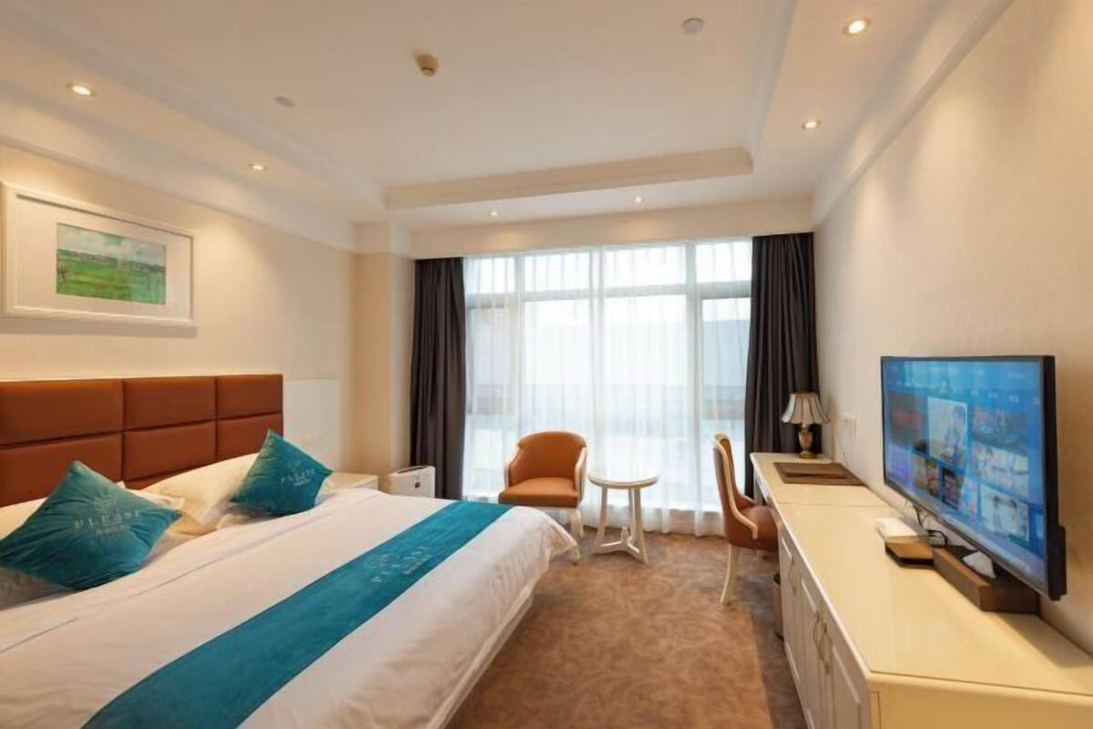 A hotel room with a large bed, a desk, a chair, a television, and a window with curtains.