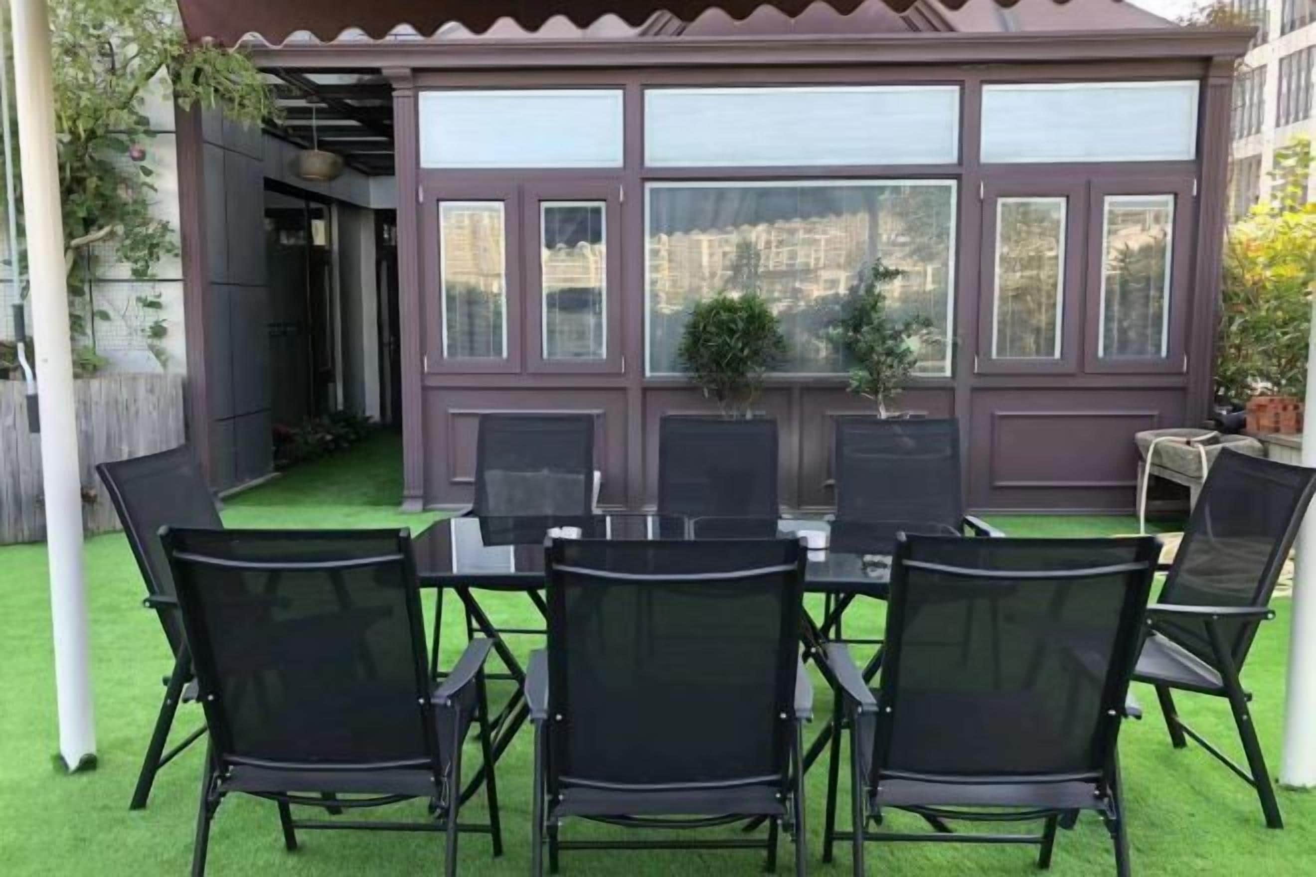 A covered patio with a table and chairs, a view of the city, and a small garden area.