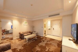 A spacious living room with a large brown patterned carpet, a white sofa, a white coffee table, and a television on a white cabinet. - Pulisi Hotel (Changshu)