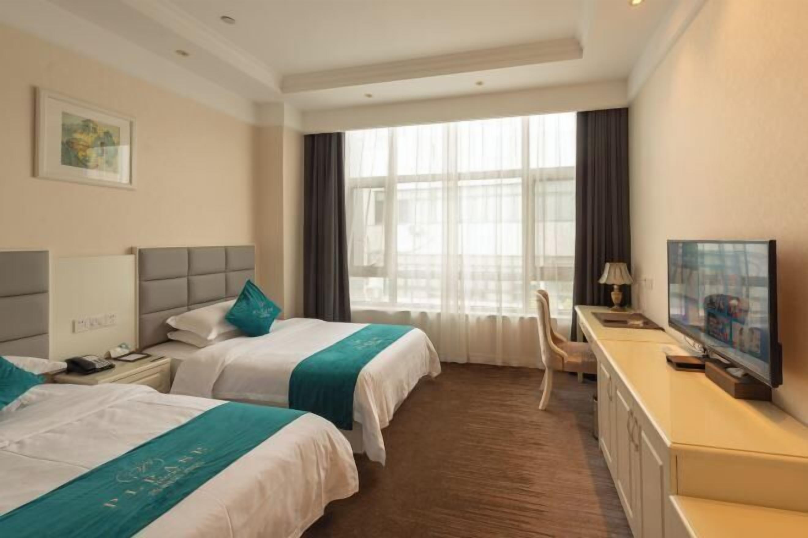 Habitación de hotel con dos camas, un escritorio con televisor y un amplio ventanal con cortinas.