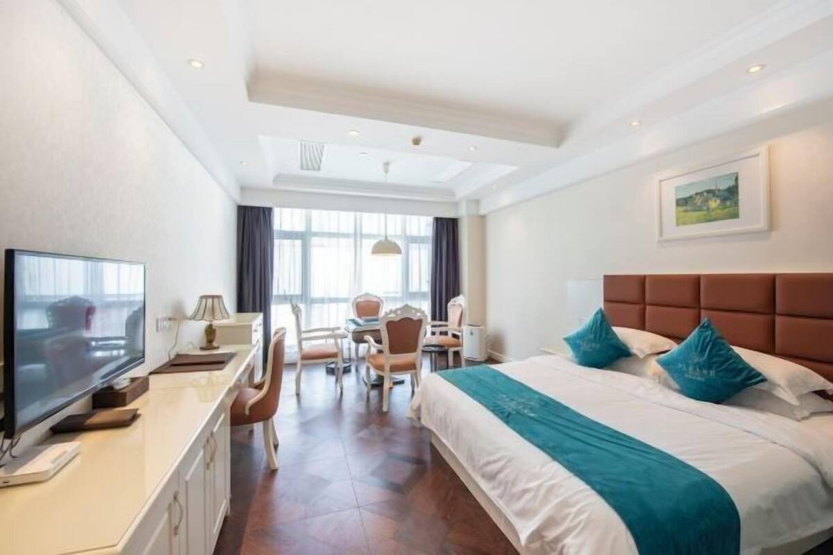 A hotel room with a large bed, a desk with a TV, a chair, and a window with curtains.
