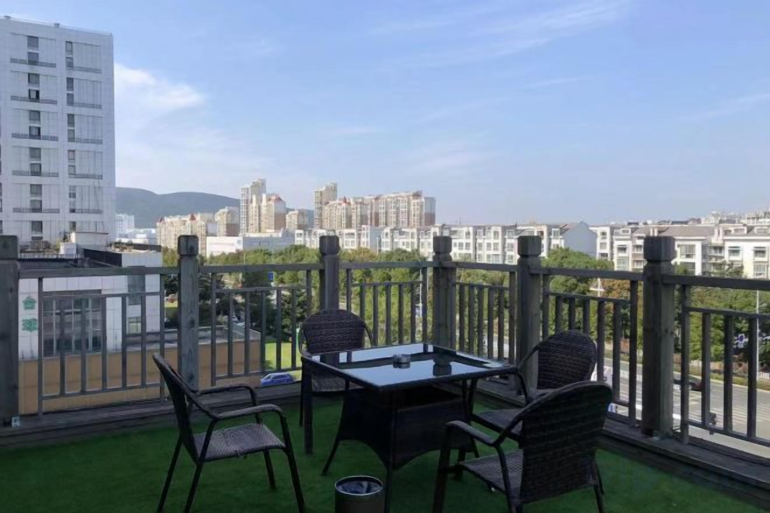Un balcón con mesa y sillas, vista a un paisaje urbano, y un edificio al fondo.