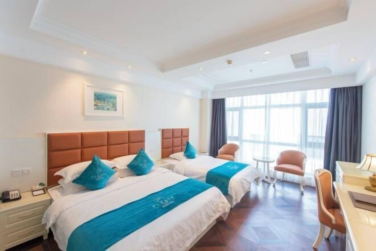 A hotel room with two beds, a desk, a chair, and a window with curtains.