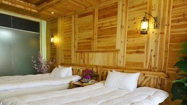 A wooden cabin room with two beds, a nightstand, and a wall-mounted lamp. - Panorama House Hotel (Guilin)