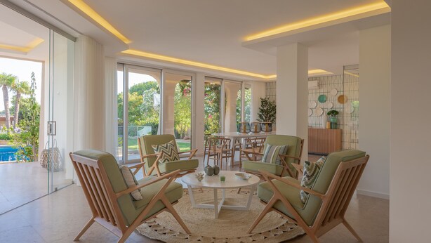 A modern living room with a round coffee table, green upholstered chairs, and a view of a pool and greenery outside. - Casa da Praia - Fantastic villa located in a privileged area just few minutes to Galé beach and large pool and garden (Galé)