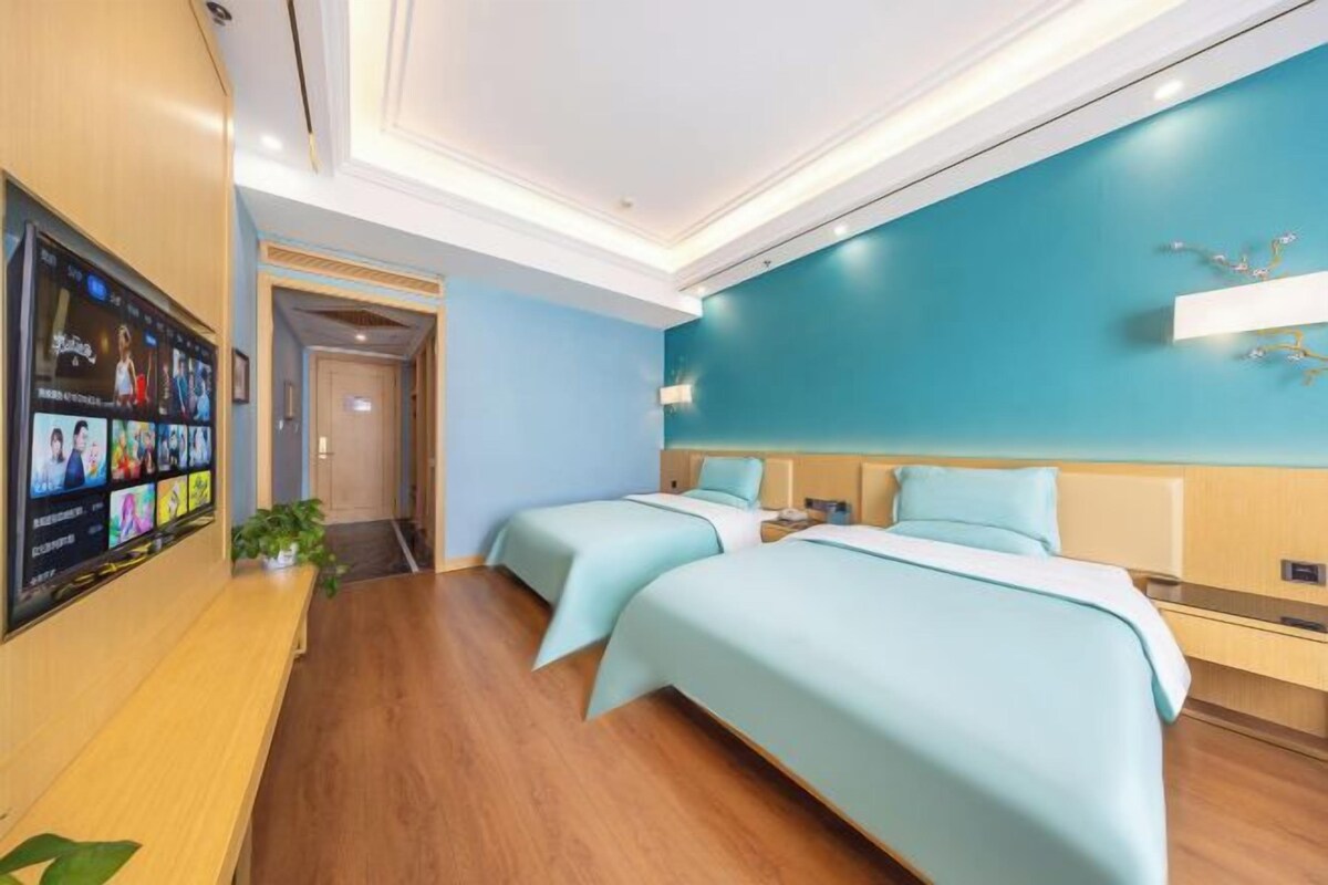 Quarto de hotel com duas camas, televisão fixada na parede e piso de madeira.
