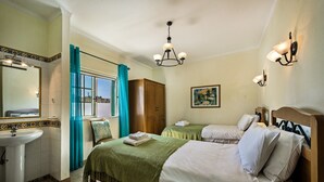 Habitación de hotel con cama, mesita de noche, espejo, ventana con cortinas, candelabro y un cuadro en la pared.