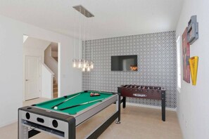 Una mesa de billar junto a una mesa de fútbolín y un televisor montado en la pared.