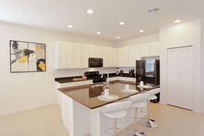 Una cocina moderna con armarios blancos, una isla central con taburetes de bar, un refrigerador de acero inoxidable y un microondas.